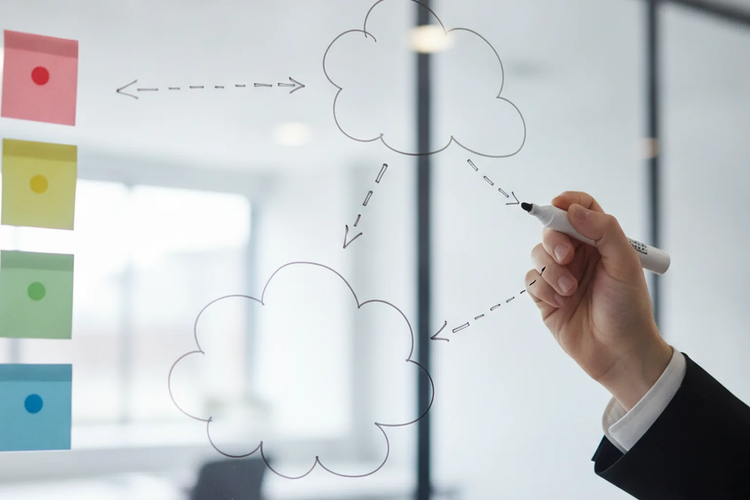 A hand drawing a cloud architecture diagram on a glass whiteboard, showing connected cloud icons to illustrate multi-cloud and integration complexity