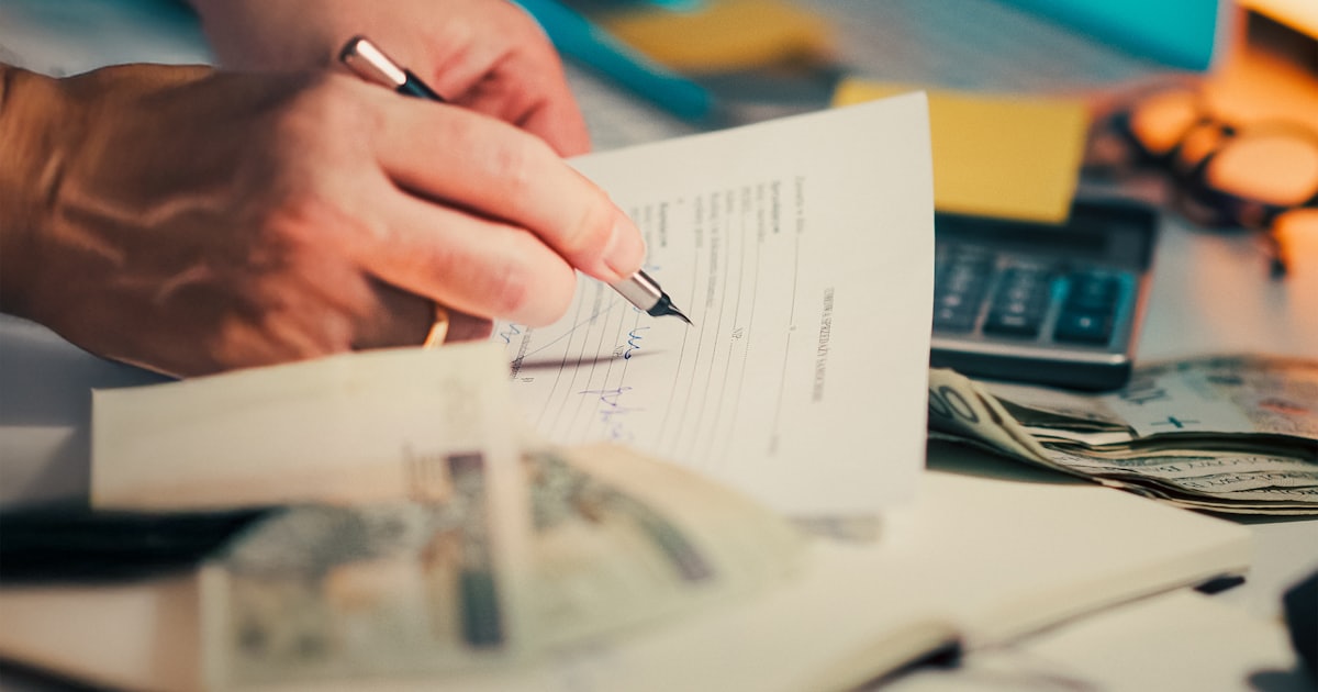 Hand signing a loan agreement with cash and calculator — loan origination software