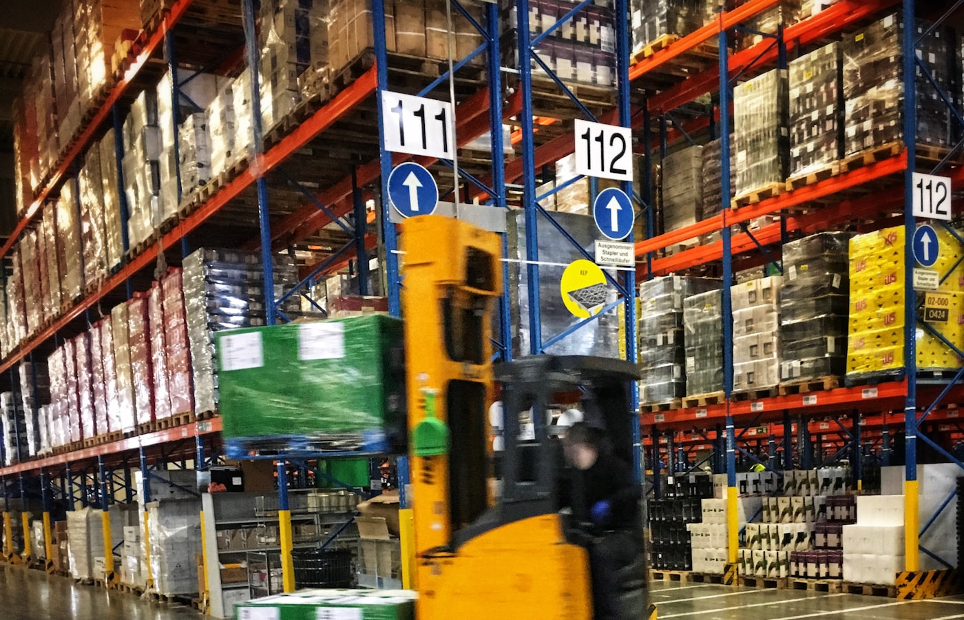 Forklift moving palletized stock through a racking aisle during putaway